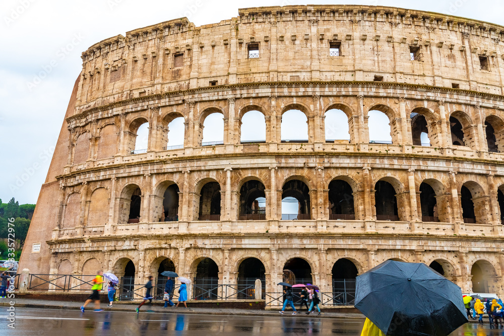 Rome, Italy. Ancient Roman Colosseum, a popular European city amphitheater landmark and tourist attraction with tourists/ people sightseeing. Historic vintage architecture ruins on rainy day.
