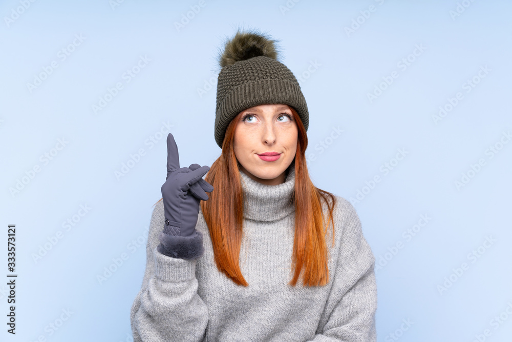 Young redhead Russian woman with winter hat over isolated blue background pointing with the index finger a great idea Young redhead Russian woman with winter hat over isolated blue background pointing with the index finger a great idea