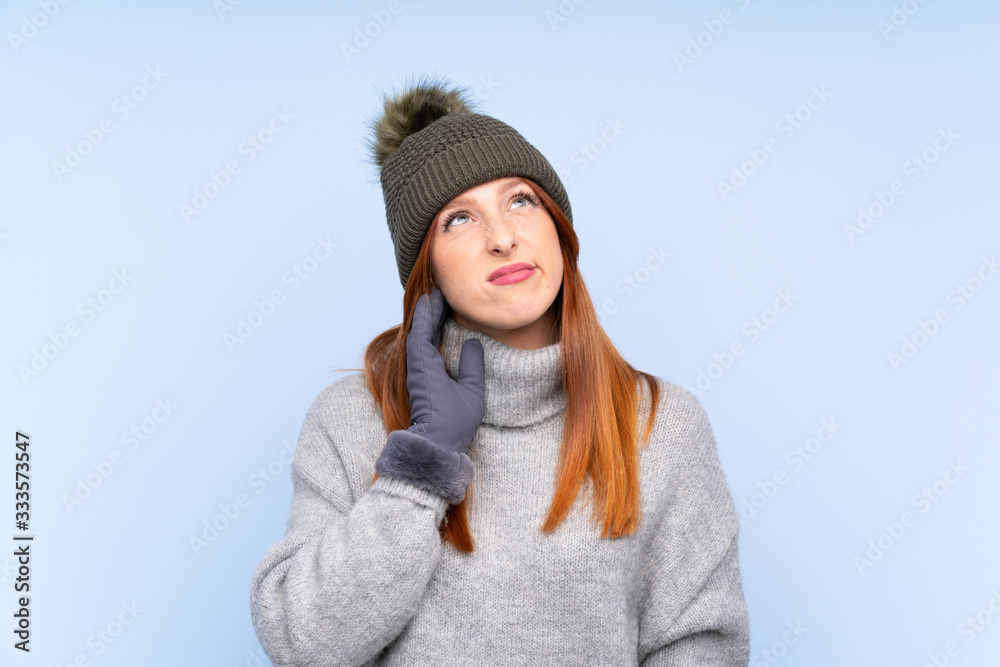 Young redhead Russian woman with winter hat over isolated blue background thinking an idea Young redhead Russian woman with winter hat over isolated blue background thinking an idea