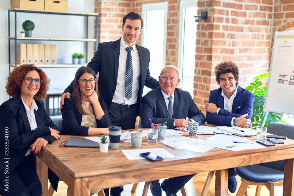 Group of business workers smiling happy and confident in a meeting. The boss standing and employees sitting with smile on face looking at the camera at the office Group of business workers smiling happy and confident in a meeting. The boss standing and employees sitting with smile on face looking at the camera at the office