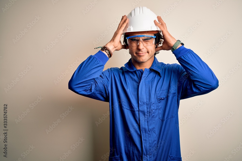 Young constructor man wearing uniform and security helmet over isolated white background suffering from headache desperate and stressed because pain and migraine. Hands on head.