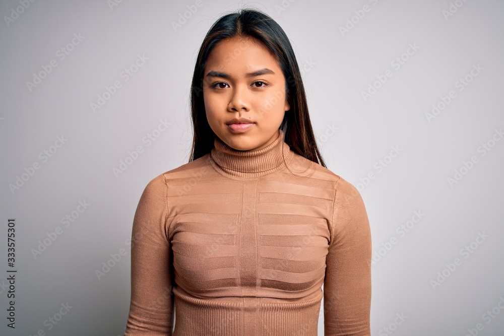 Fototapeta premium Young beautiful asian girl wearing casual turtleneck sweater standing over white background with serious expression on face. Simple and natural looking at the camera.