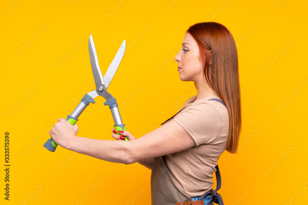 Young redhead gardener woman withpruning shears over isolated yellow background Young redhead gardener woman withpruning shears over isolated yellow background