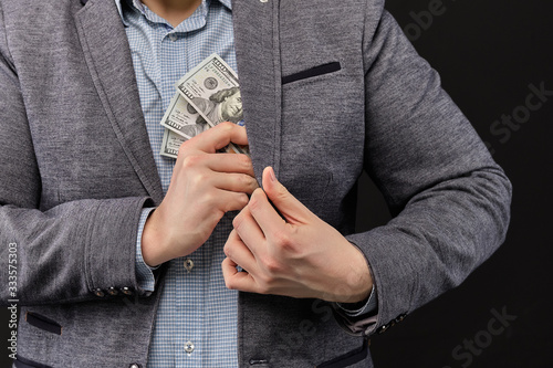 A man in a jacket puts dollars in his pocket on a black background.