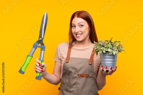 Slika na platnu Young redhead gardener woman withpruning shears over isolated yellow background