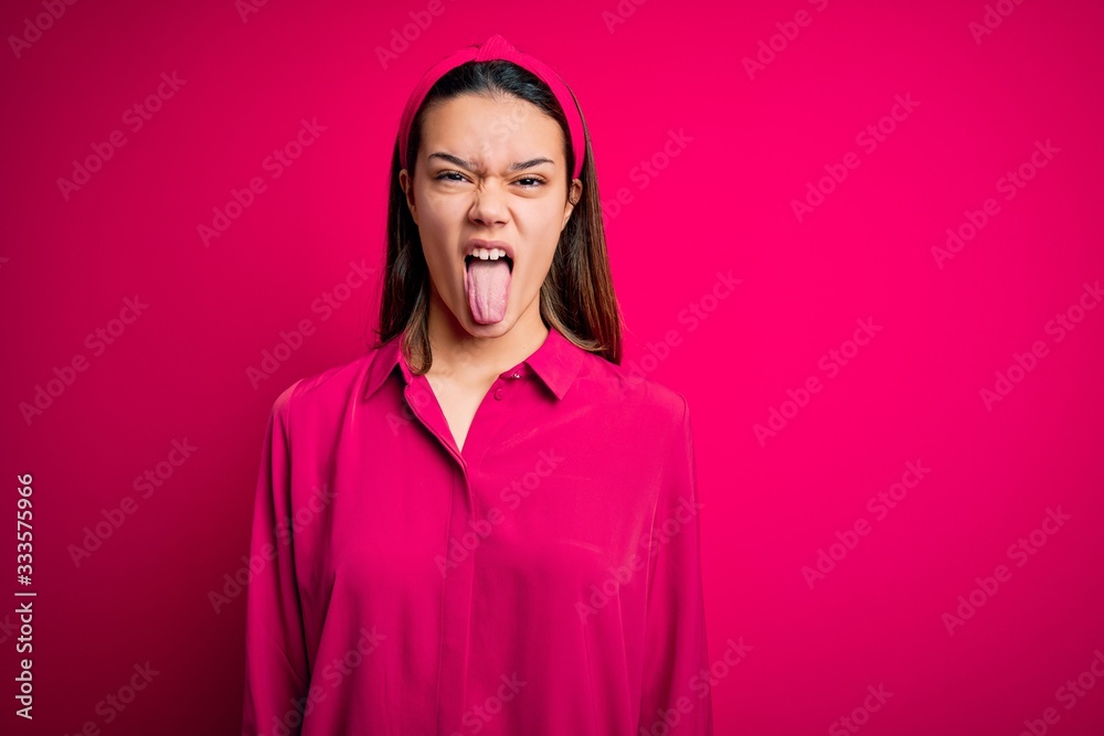 Young beautiful brunette girl wearing casual shirt standing over isolated pink background sticking tongue out happy with funny expression. Emotion concept. Young beautiful brunette girl wearing casual shirt standing over isolated pink background sticking tongue out happy with funny expression. Emotion concept.