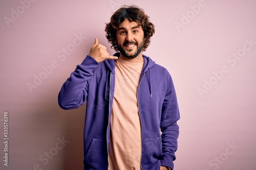Young handsome sporty man with beard wearing casual sweatshirt over pink background smiling doing phone gesture with hand and fingers like talking on the telephone. Communicating concepts. © Krakenimages.com