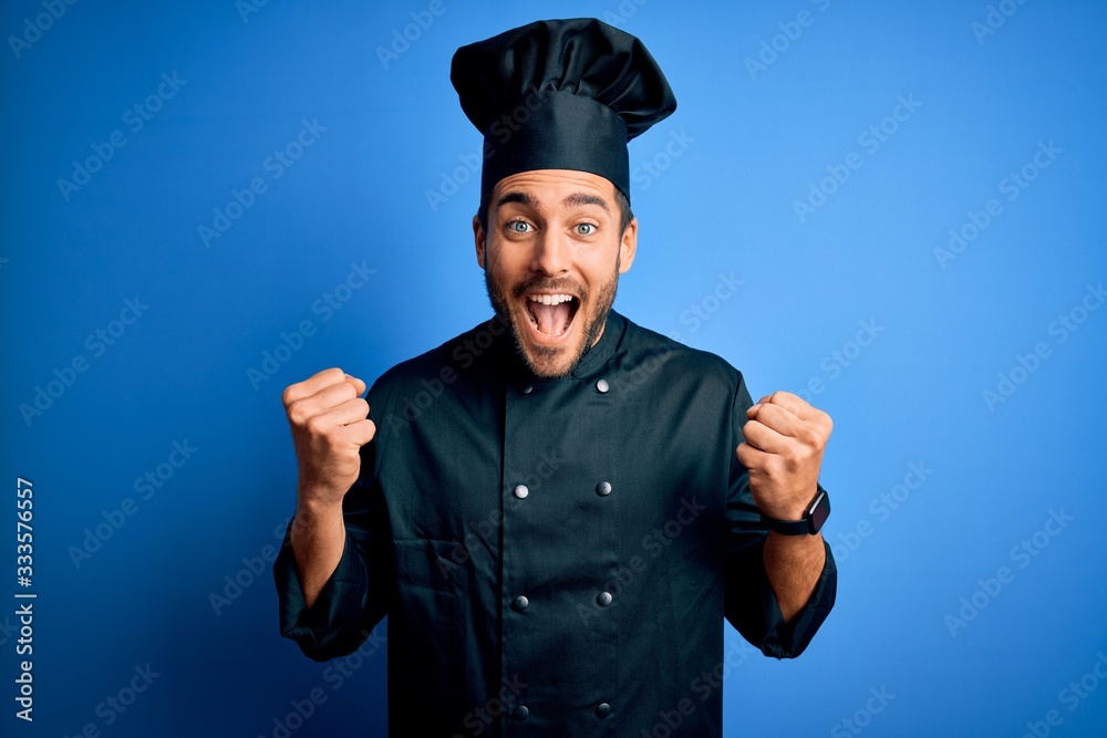 Young handsome chef man with beard wearing cooker uniform and hat over blue background celebrating surprised and amazed for success with arms raised and open eyes. Winner concept. Young handsome chef man with beard wearing cooker uniform and hat over blue background celebrating surprised and amazed for success with arms raised and open eyes. Winner concept.
