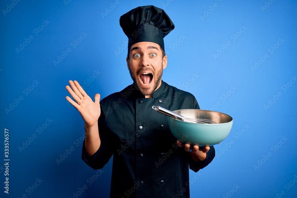 Young cooker man with beard wearing uniform using whisk and bowl over blue background very happy and excited, winner expression celebrating victory screaming with big smile and raised hands Young cooker man with beard wearing uniform using whisk and bowl over blue background very happy and excited, winner expression celebrating victory screaming with big smile and raised hands
