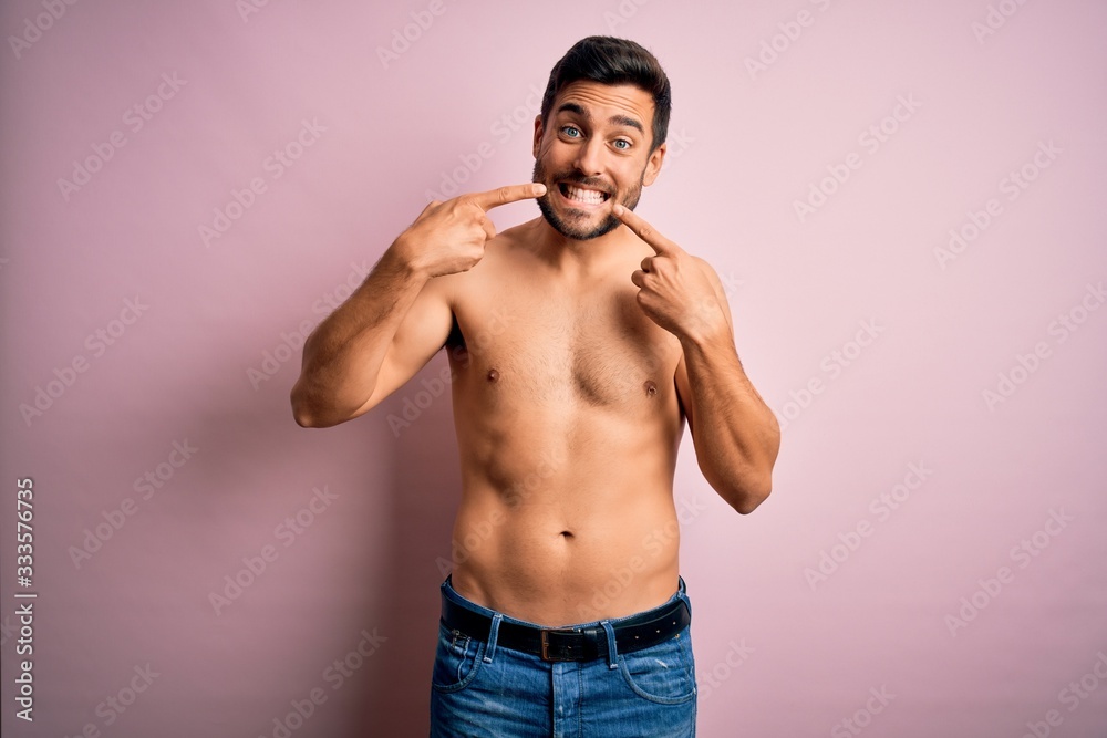 Fototapeta premium Young handsome strong man with beard shirtless standing over isolated pink background smiling cheerful showing and pointing with fingers teeth and mouth. Dental health concept.