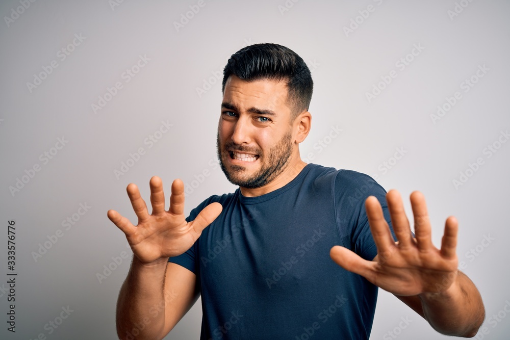 Young handsome man wearing casual t-shirt standing over isolated white background afraid and terrified with fear expression stop gesture with hands, shouting in shock. Panic concept.