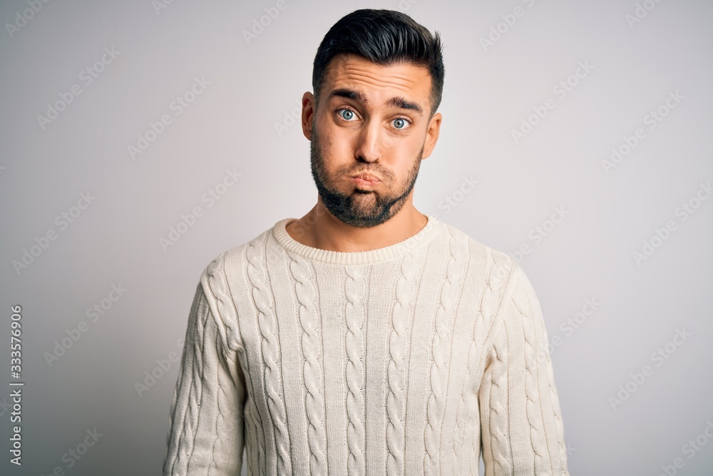 Young handsome man wearing casual sweater standing over isolated white background puffing cheeks with funny face. Mouth inflated with air, crazy expression.