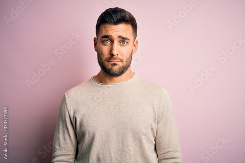 Young handsome man wearing casual sweater standing over isolated pink background depressed and worry for distress, crying angry and afraid. Sad expression.