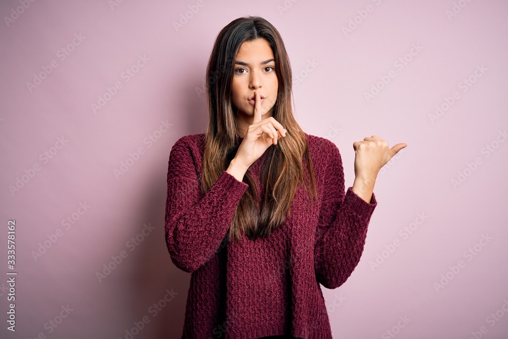 Young beautiful girl wearing casual sweater over isolated pink background asking to be quiet with finger on lips pointing with hand to the side. Silence and secret concept. Young beautiful girl wearing casual sweater over isolated pink background asking to be quiet with finger on lips pointing with hand to the side. Silence and secret concept.