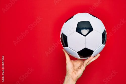 Beautiful hand of man holding football ball over isolated red background