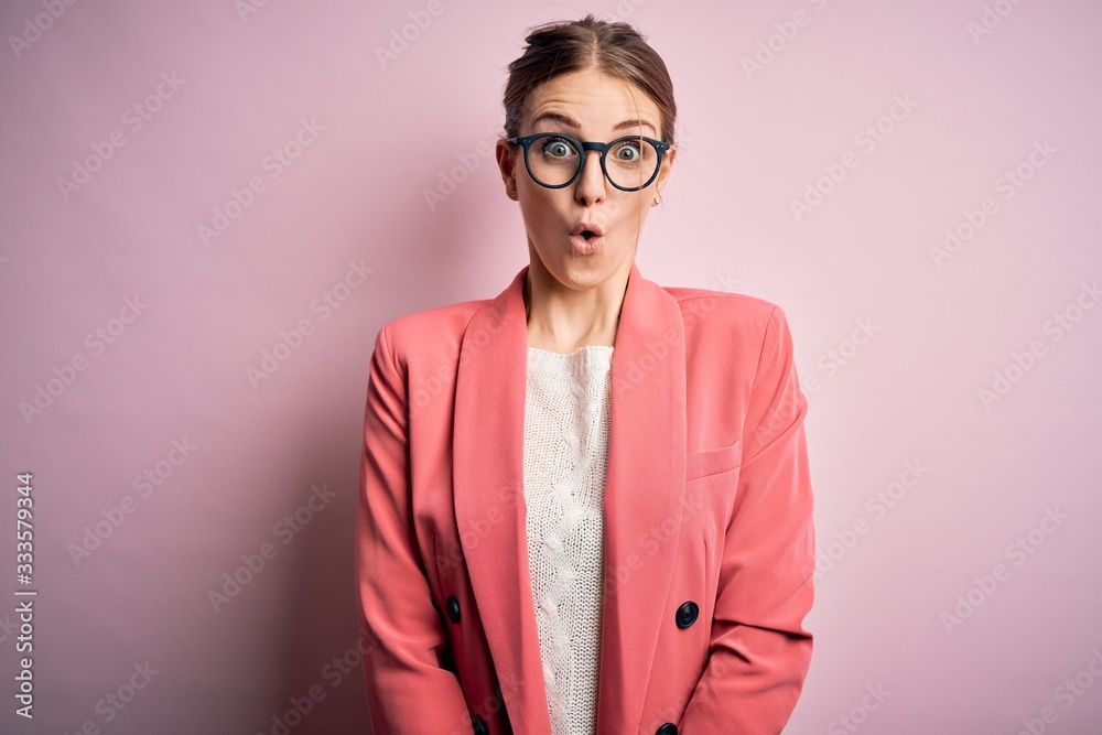 Young beautiful redhead woman wearing jacket and glasses over isolated pink background afraid and shocked with surprise expression, fear and excited face.
