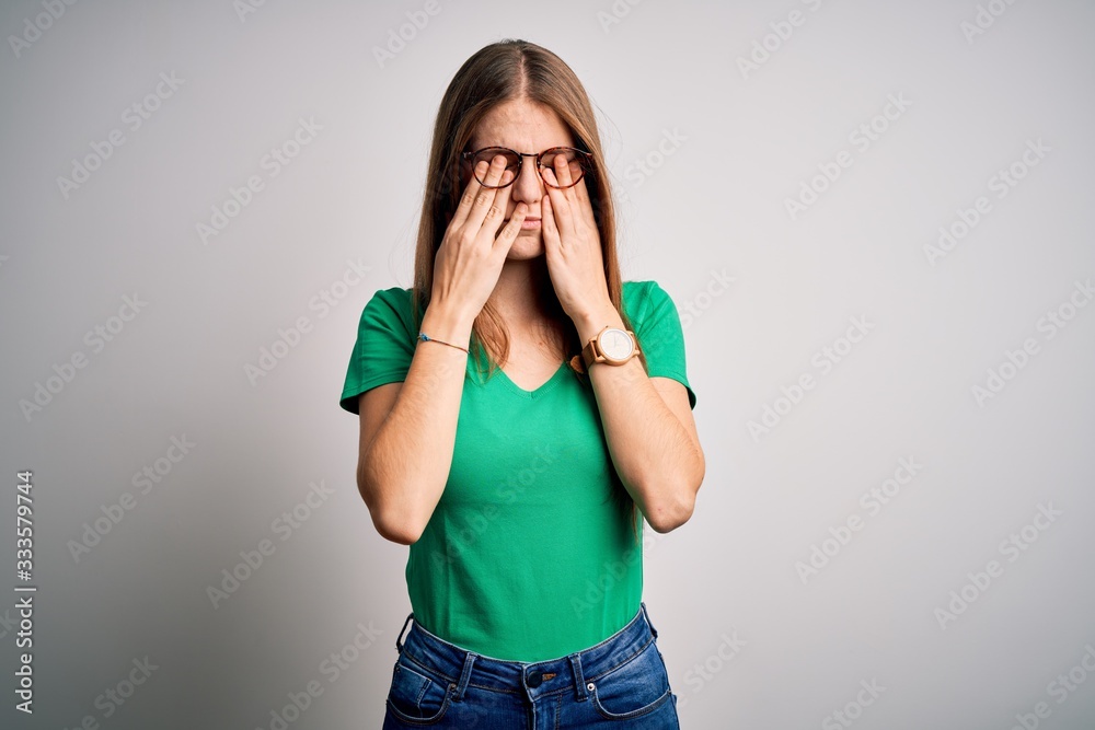 Young beautiful redhead woman wearing casual green t-shirt and glasses over white background rubbing eyes for fatigue and headache, sleepy and tired expression. Vision problem Young beautiful redhead woman wearing casual green t-shirt and glasses over white background rubbing eyes for fatigue and headache, sleepy and tired expression. Vision problem