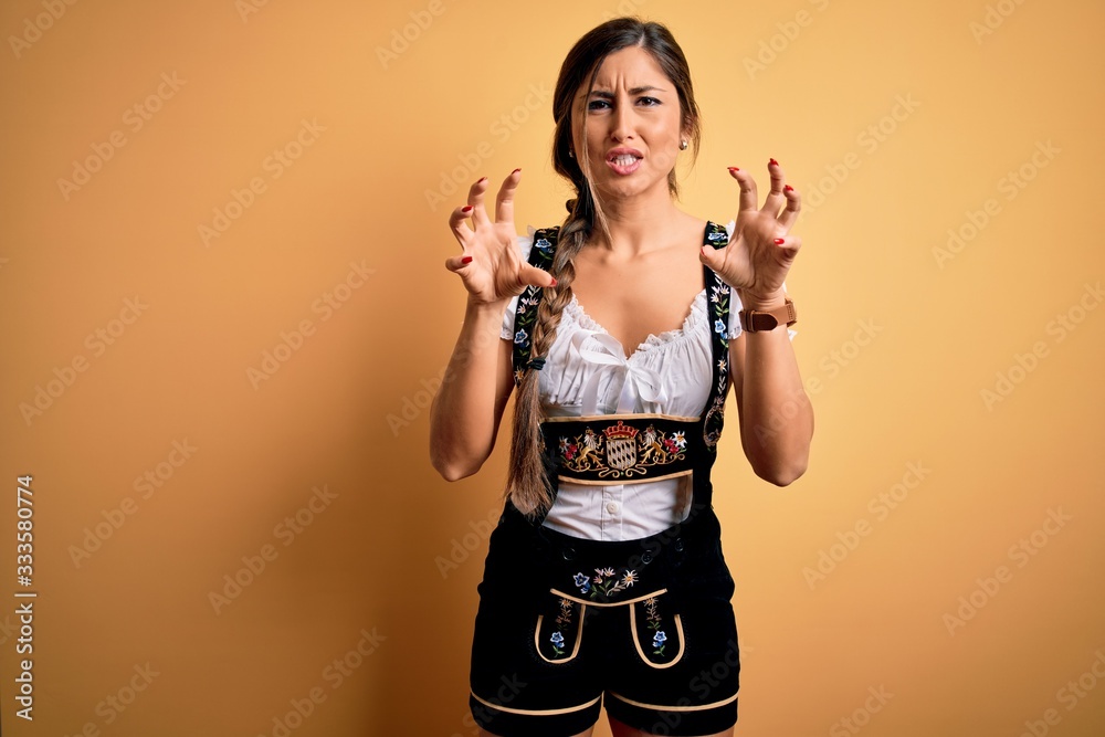 Young beautiful brunette german woman celebrating Octoberfest wearing traditional dress smiling funny doing claw gesture as cat, aggressive and sexy expression