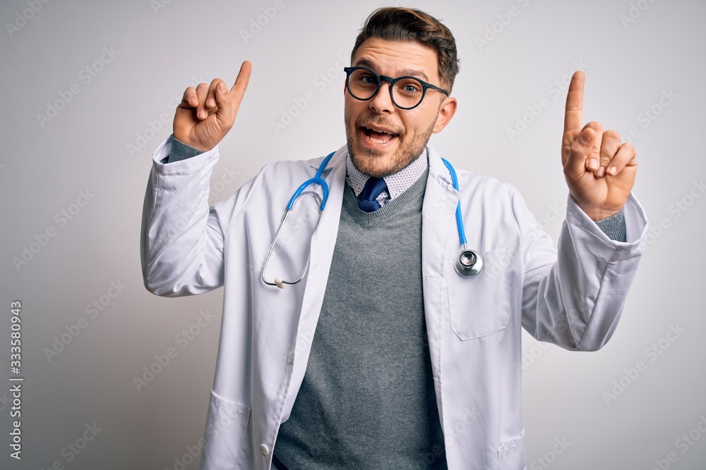 Young doctor man with blue eyes wearing medical coat and stethoscope over isolated background smiling amazed and surprised and pointing up with fingers and raised arms. Young doctor man with blue eyes wearing medical coat and stethoscope over isolated background smiling amazed and surprised and pointing up with fingers and raised arms.