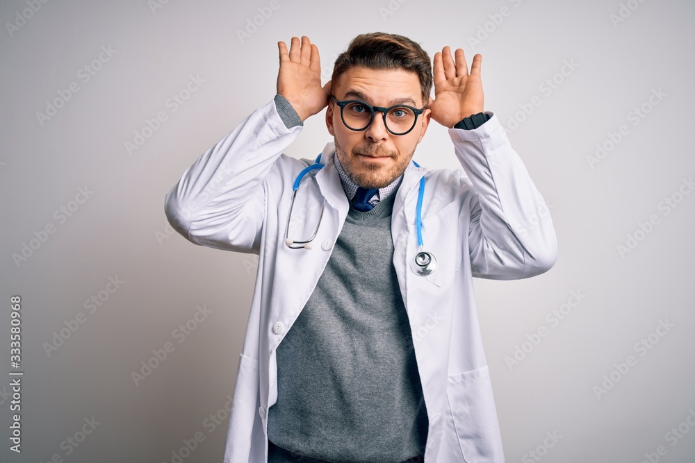 Young doctor man with blue eyes wearing medical coat and stethoscope over isolated background Doing bunny ears gesture with hands palms looking cynical and skeptical. Easter rabbit concept. Young doctor man with blue eyes wearing medical coat and stethoscope over isolated background Doing bunny ears gesture with hands palms looking cynical and skeptical. Easter rabbit concept.