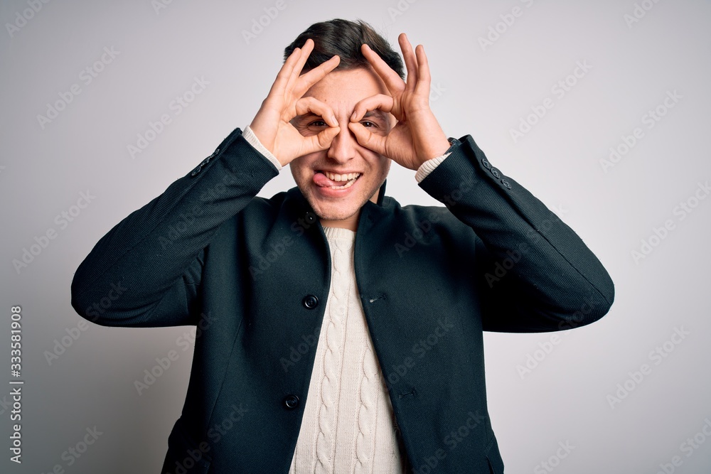 Young handsome business mas wearing elegant winter coat standing over isolated background doing ok gesture like binoculars sticking tongue out, eyes looking through fingers. Crazy expression. Young handsome business mas wearing elegant winter coat standing over isolated background doing ok gesture like binoculars sticking tongue out, eyes looking through fingers. Crazy expression.