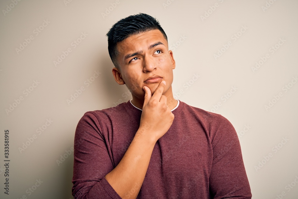 Young handsome latin man wearing casual sweater standing over isolated white background with hand on chin thinking about question, pensive expression. Smiling with thoughtful face. Doubt concept. Young handsome latin man wearing casual sweater standing over isolated white background with hand on chin thinking about question, pensive expression. Smiling with thoughtful face. Doubt concept.