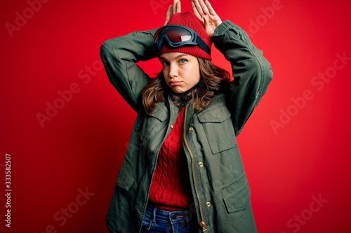 Fotografía Young blonde girl wearing ski glasses and winter coat for ski weather over red background Doing bunny ears gesture with hands palms looking cynical and skeptical