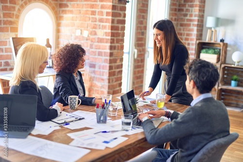 Group of business workers smiling happy and confident. Working together with smile on face. Young beautiful woman standing explaining documents at the office photo
