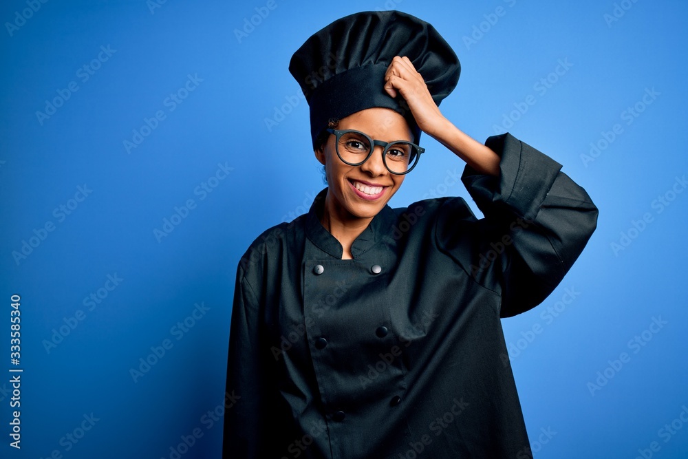 Young african american chef woman wearing cooker uniform and hat over blue background smiling confident touching hair with hand up gesture, posing attractive and fashionable Young african american chef woman wearing cooker uniform and hat over blue background smiling confident touching hair with hand up gesture, posing attractive and fashionable