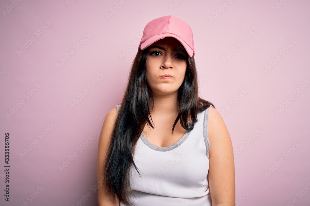 Young brunette woman wearing casual sport cap over pink background skeptic and nervous, frowning upset because of problem. Negative person. Young brunette woman wearing casual sport cap over pink background skeptic and nervous, frowning upset because of problem. Negative person.