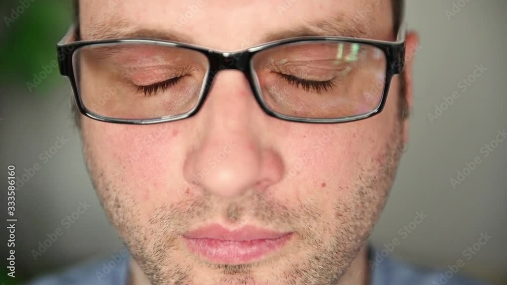 A handsome guy in glasses with blue eyes looks at the camera. Uses glasses and rubs his eyes A handsome guy in glasses with blue eyes looks at the camera. Uses glasses and rubs his eyes