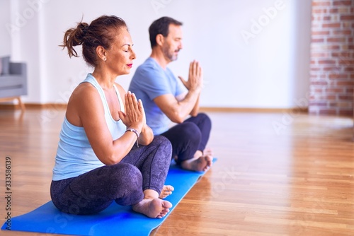 Middle age beautiful sporty couple sitting on mat practicing yoga doing prayer pose at gym