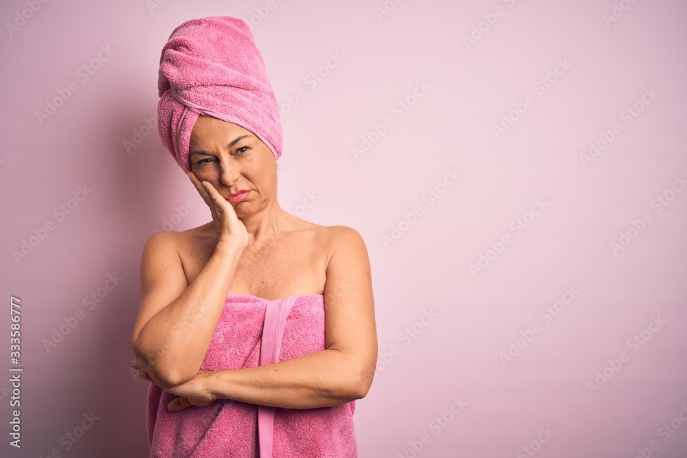 Middle age woman wearing bath towel from beauty body care over pink background thinking looking tired and bored with depression problems with crossed arms. Middle age woman wearing bath towel from beauty body care over pink background thinking looking tired and bored with depression problems with crossed arms.