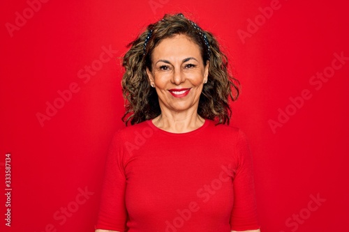 Middle age senior brunette woman wearing casual t-shirt standing over red background with a happy and cool smile on face. Lucky person.