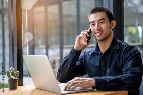 a smliling businessman talking on a phone while sitting in front of a laptop. photo