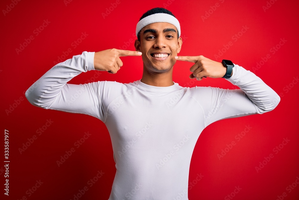Fototapeta premium Young handsome african american sportsman wearing sportswear over red background smiling cheerful showing and pointing with fingers teeth and mouth. Dental health concept.