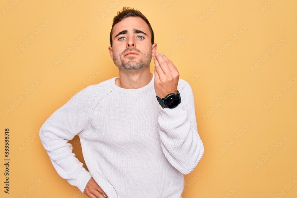 Young handsome man with blue eyes wearing casual sweater standing over yellow background Doing Italian gesture with hand and fingers confident expression Young handsome man with blue eyes wearing casual sweater standing over yellow background Doing Italian gesture with hand and fingers confident expression