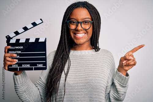 Young african american director girl filming a movie using clapboard over isolated background very happy pointing with hand and finger to the side photo