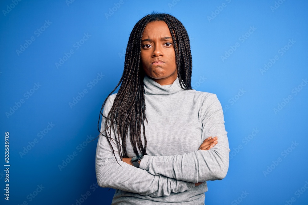 Young african american woman standing wearing casual turtleneck over blue isolated background skeptic and nervous, disapproving expression on face with crossed arms. Negative person. Young african american woman standing wearing casual turtleneck over blue isolated background skeptic and nervous, disapproving expression on face with crossed arms. Negative person.