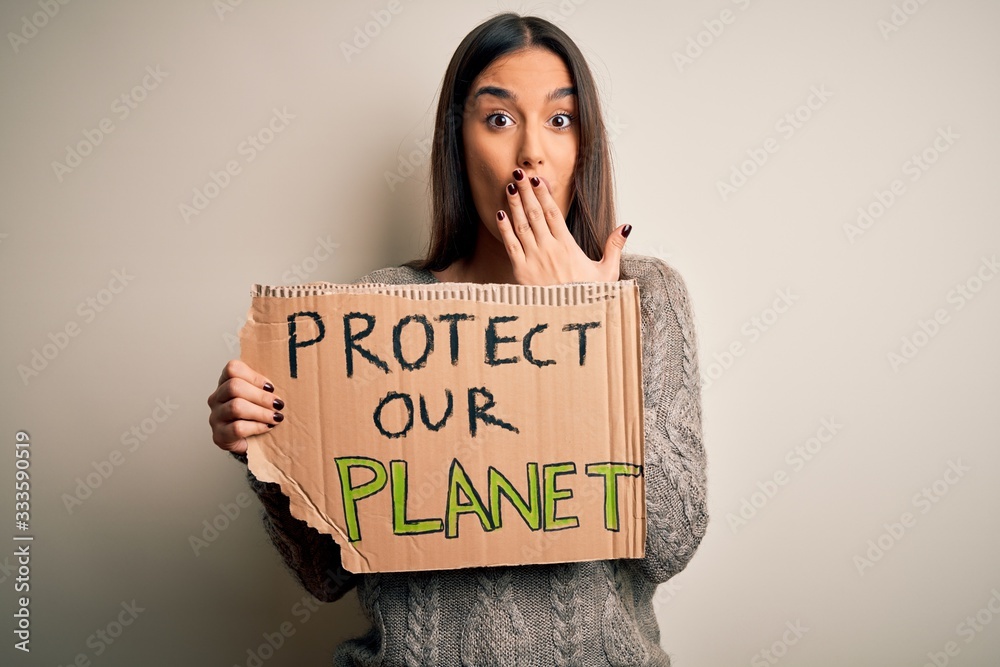 Young beautiful brunette activist woman protesting for protect our planet holding poster cover mouth with hand shocked with shame for mistake, expression of fear, scared in silence, secret concept Young beautiful brunette activist woman protesting for protect our planet holding poster cover mouth with hand shocked with shame for mistake, expression of fear, scared in silence, secret concept