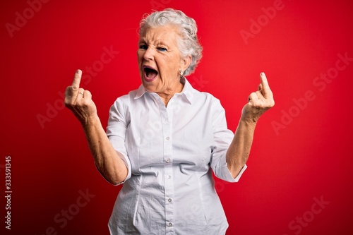 Senior beautiful woman wearing elegant shirt standing over isolated red background Showing middle finger doing fuck you bad expression, provocation and rude attitude. Screaming excited