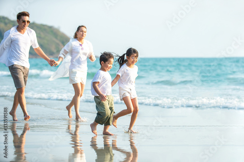 Smiling Young Asian happy family parents with child running and having fun together on the beach in summertime. Father, mother and kids relax and enjoy summer lifestyle travel holiday vacation.