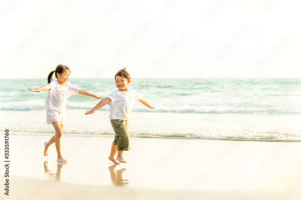 Happy little Asian brother and sister running and playing with smiling and laughing together on the beach at sunset. Adorable kids girl and boy relax and having fun in summer holiday vacation travel.