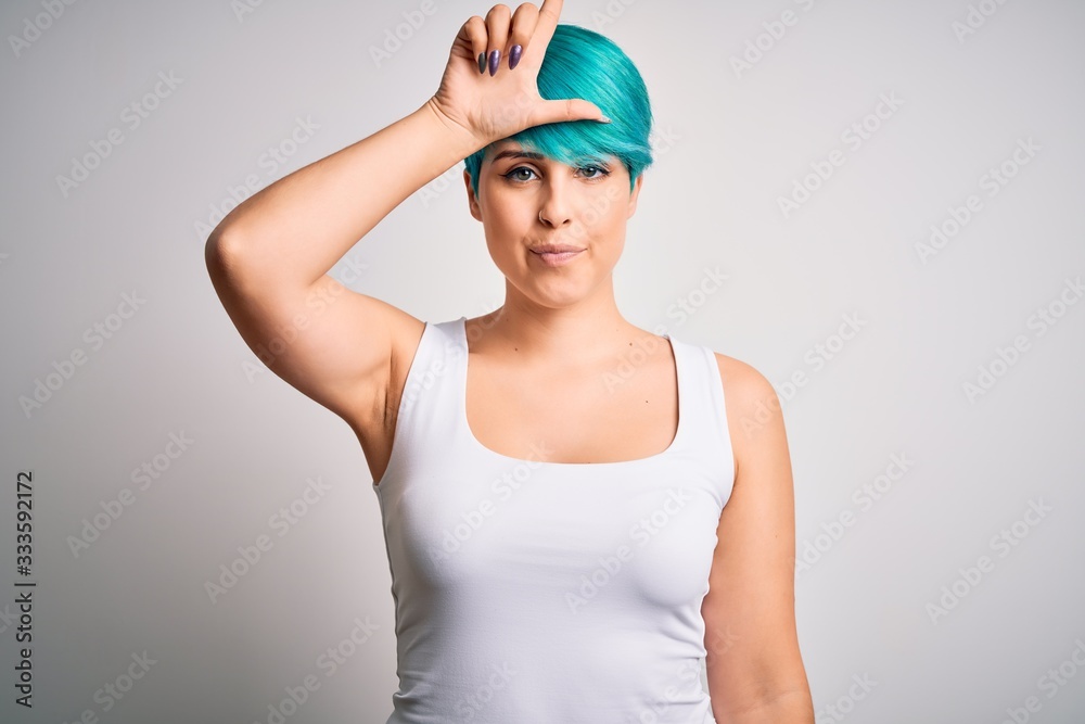 Young beautiful woman with blue fashion hair wearing casual t-shirt over white background making fun of people with fingers on forehead doing loser gesture mocking and insulting. Young beautiful woman with blue fashion hair wearing casual t-shirt over white background making fun of people with fingers on forehead doing loser gesture mocking and insulting.