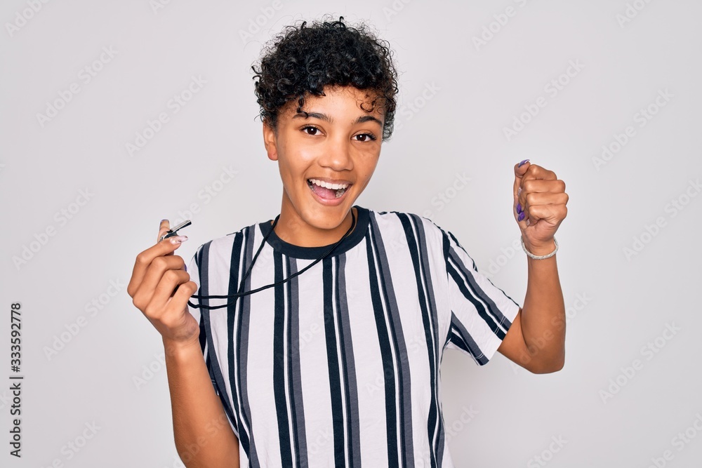 Young beautiful african american afro referee woman wearing striped uniform using whistle screaming proud and celebrating victory and success very excited, cheering emotion