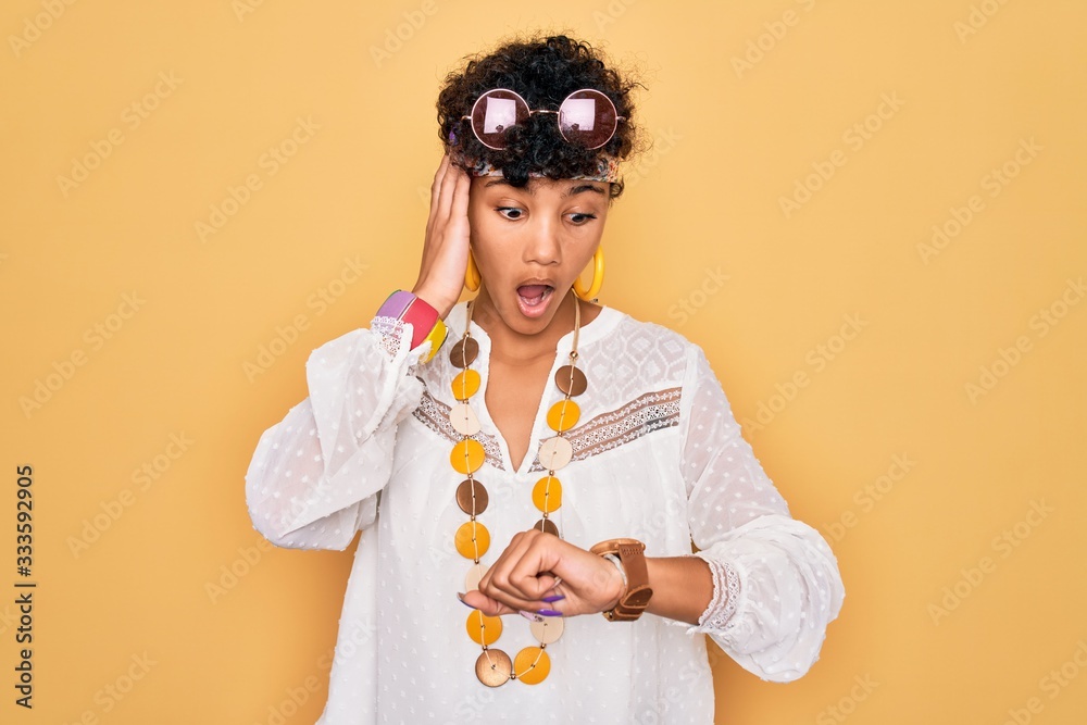 Young beautiful african american afro hippie woman wearing sunglasses and accessories Looking at the watch time worried, afraid of getting late