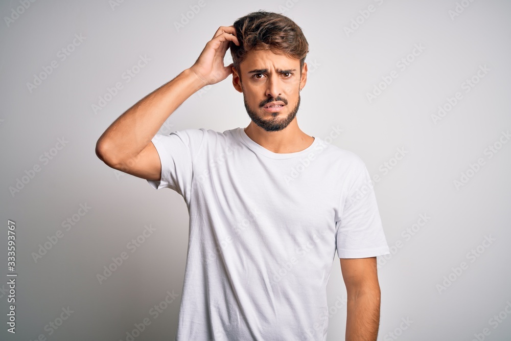 Young handsome man with beard wearing casual t-shirt standing over white background confuse and wonder about question. Uncertain with doubt, thinking with hand on head. Pensive concept. Young handsome man with beard wearing casual t-shirt standing over white background confuse and wonder about question. Uncertain with doubt, thinking with hand on head. Pensive concept.