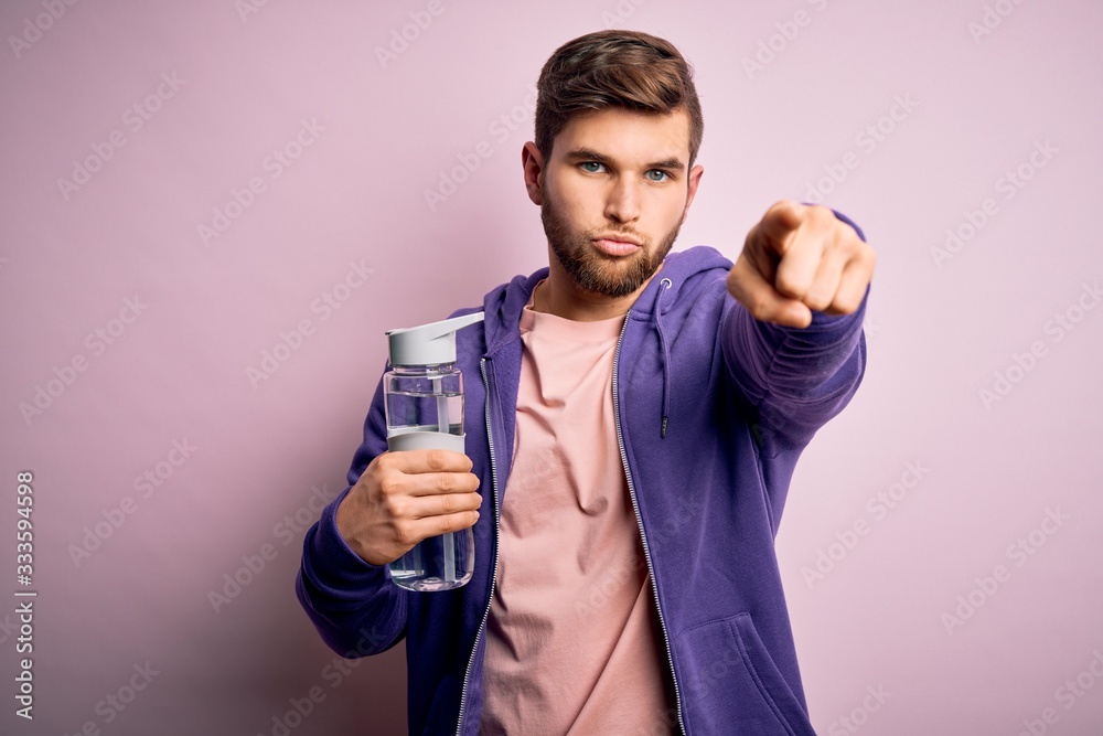Young blond sporty man with beard and blue eyes doing sport holding bottle of water pointing with finger to the camera and to you, hand sign, positive and confident gesture from the front Young blond sporty man with beard and blue eyes doing sport holding bottle of water pointing with finger to the camera and to you, hand sign, positive and confident gesture from the front