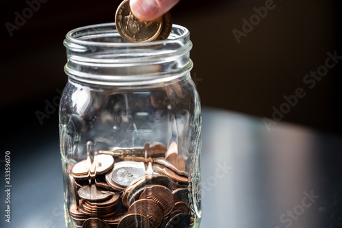 Two fingers holding coins to be dropped into a glass jar photo