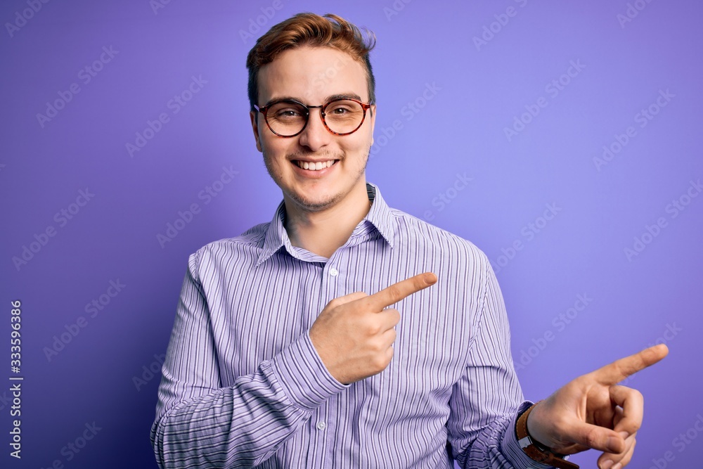 Young handsome redhead man wearing casual shirt and glasses over purple background smiling and looking at the camera pointing with two hands and fingers to the side. Young handsome redhead man wearing casual shirt and glasses over purple background smiling and looking at the camera pointing with two hands and fingers to the side.